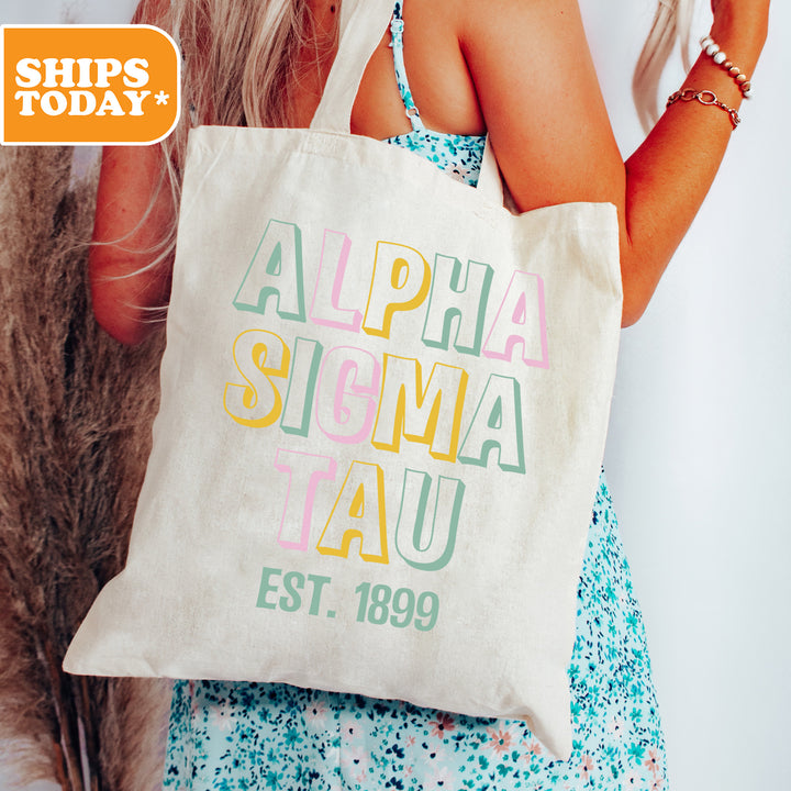 a woman holding a tote bag with the words alpha sigma tau