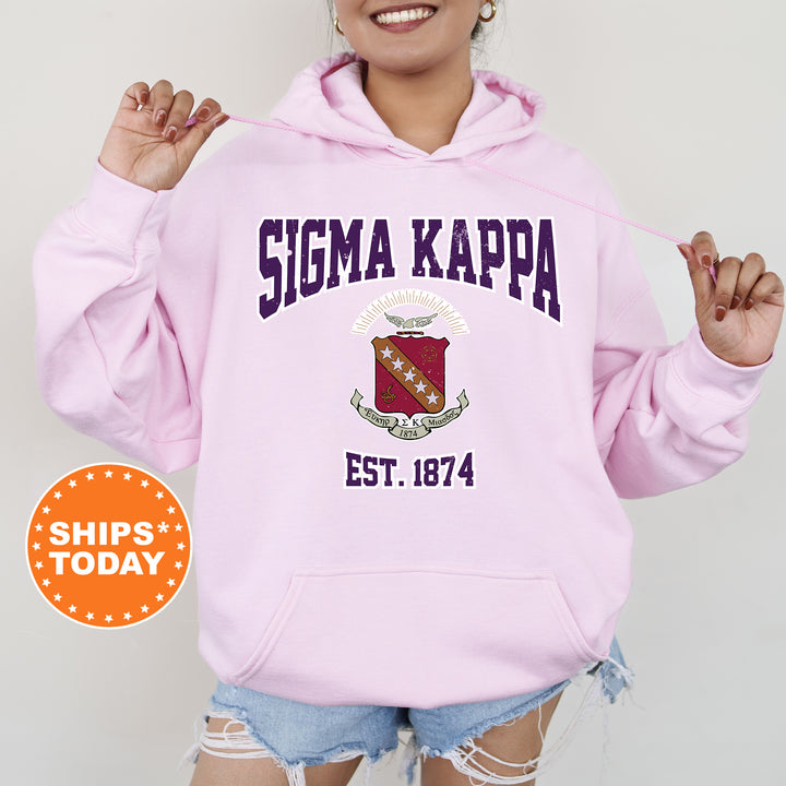 a woman wearing a pink hoodie with a crest on it