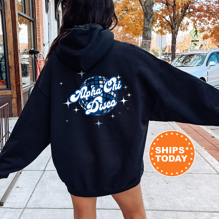 A person wearing a black hoodie with the text "Alpha Chi Diced" printed on it, standing on a sidewalk with a car and a building in the background.