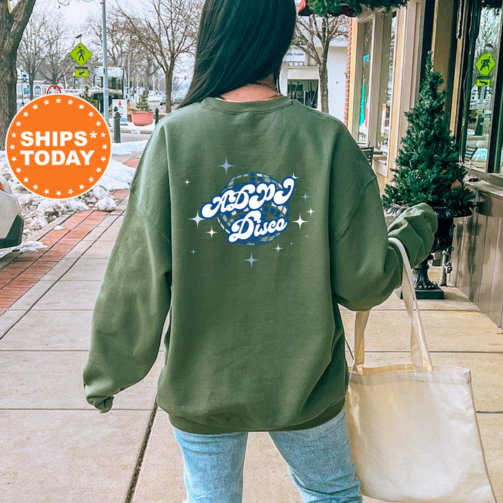 A person wearing a green sweatshirt with a graphic design on the back is walking down a sidewalk, carrying a white bag.