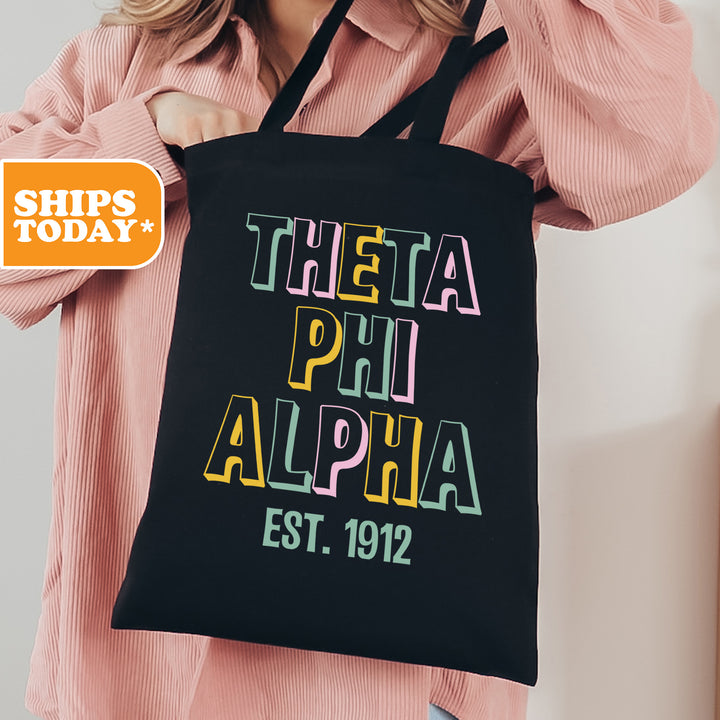 a woman holding a black tote bag with the words thera phi alpha