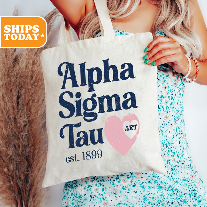 a woman holding a tote bag with the words alpha sigma tau