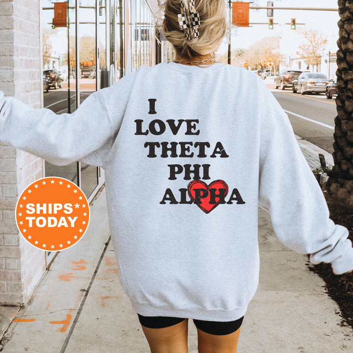 a woman walking down a sidewalk wearing a sweatshirt that says i love thea phi