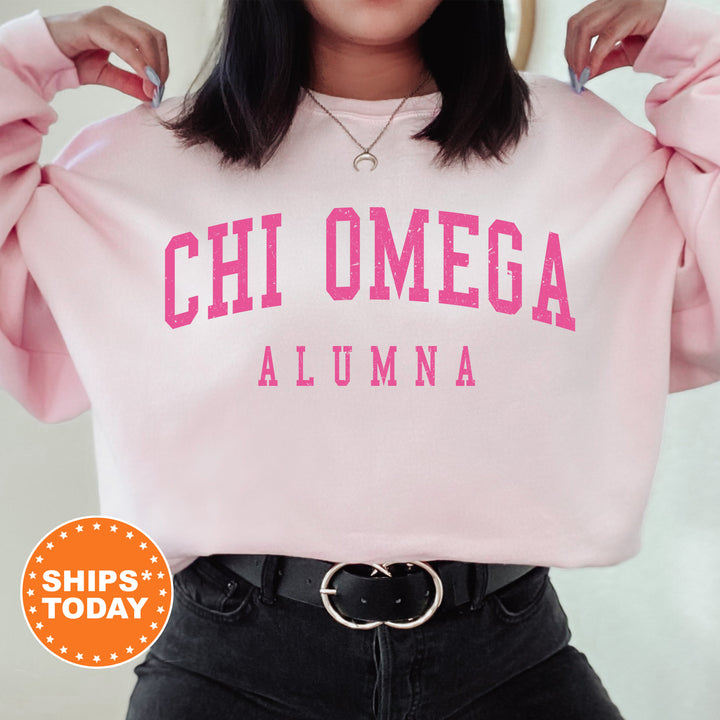 a woman wearing a pink sweatshirt with the words chi omega on it