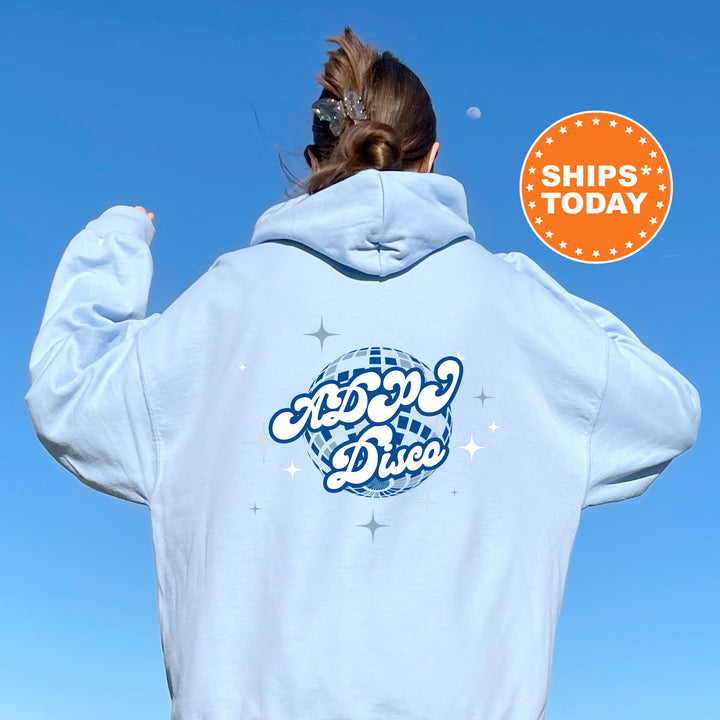 A person wearing a light blue hoodie with a graphic design on the back, standing against a clear blue sky.
