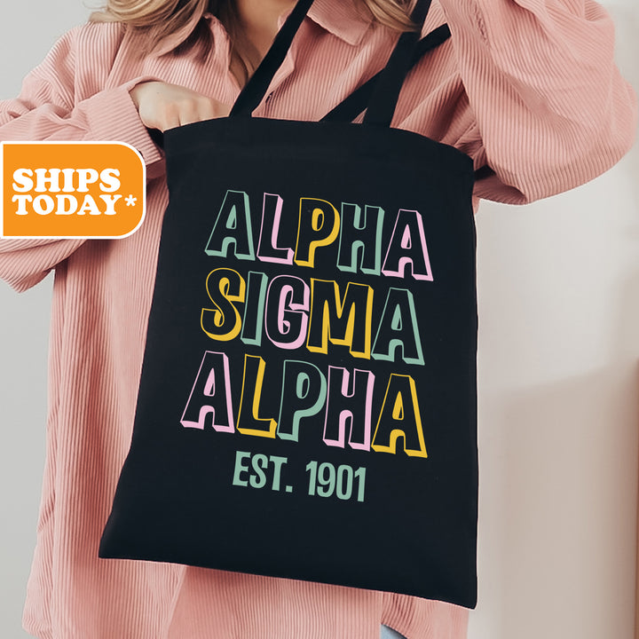 a woman holding a black tote bag with the words, alpha, sigma,