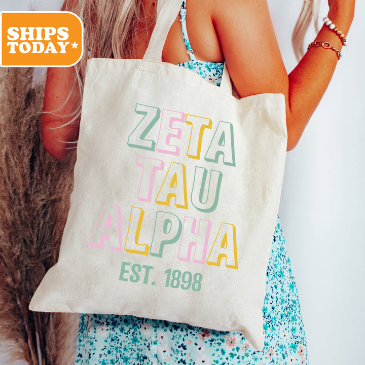 a woman holding a tote bag with the words zeta tau alpa est