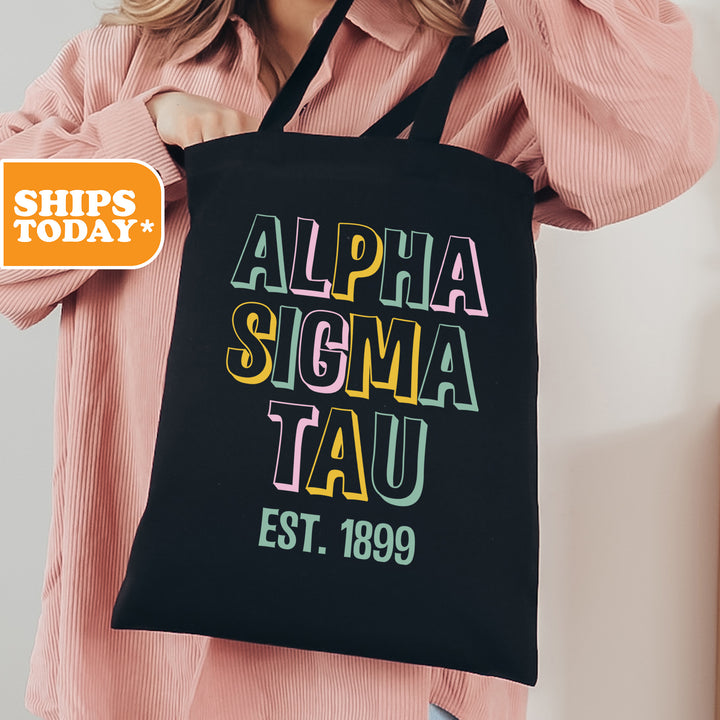 a woman holding a black tote bag with the words, alpha sigma tau est