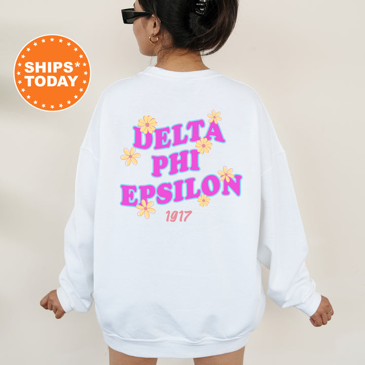 A woman wearing a white sweatshirt with the Delta Phi Epsilon logo and text printed on it.