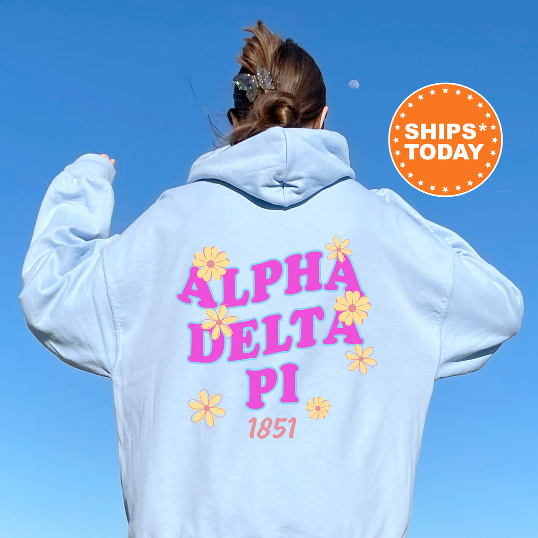A person wearing a light blue hoodie with the text "ALPA DELTA PI 1851" printed on it, standing against a clear blue sky.