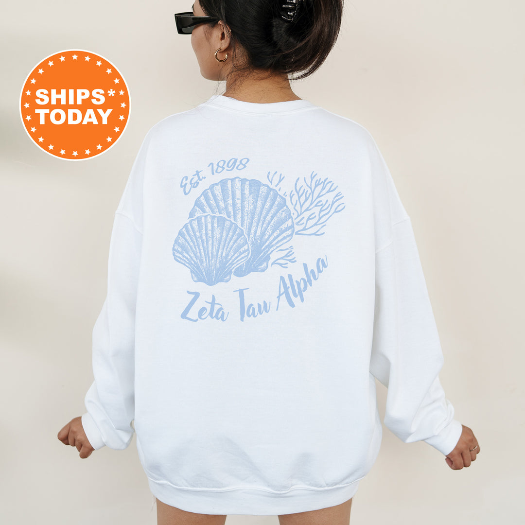 A woman wearing a white sweatshirt with a graphic design of two seashells and the text "Zeta Taw Alpha" printed on it.