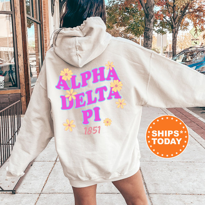 A person wearing a white hoodie with the text "ALPHA DELTA PI" printed on it, standing on a sidewalk.