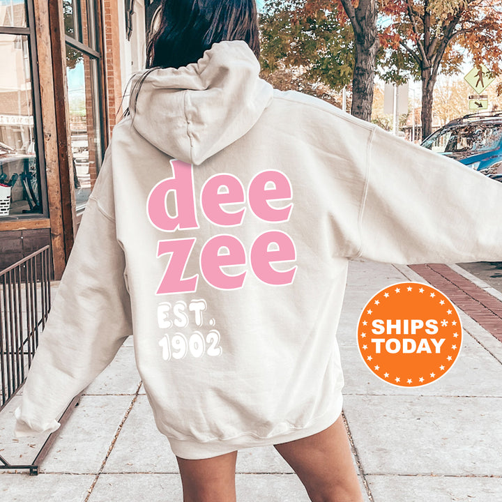 A person wearing a white hoodie with the text "dee zee" printed on it, standing on a sidewalk.