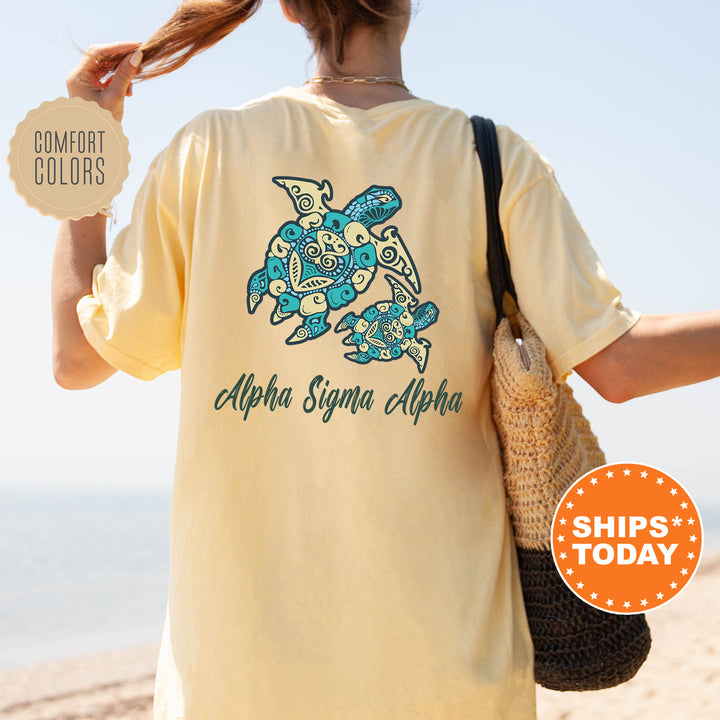 A person wearing a yellow t-shirt with a turtle design and text, standing on a beach with a handbag.