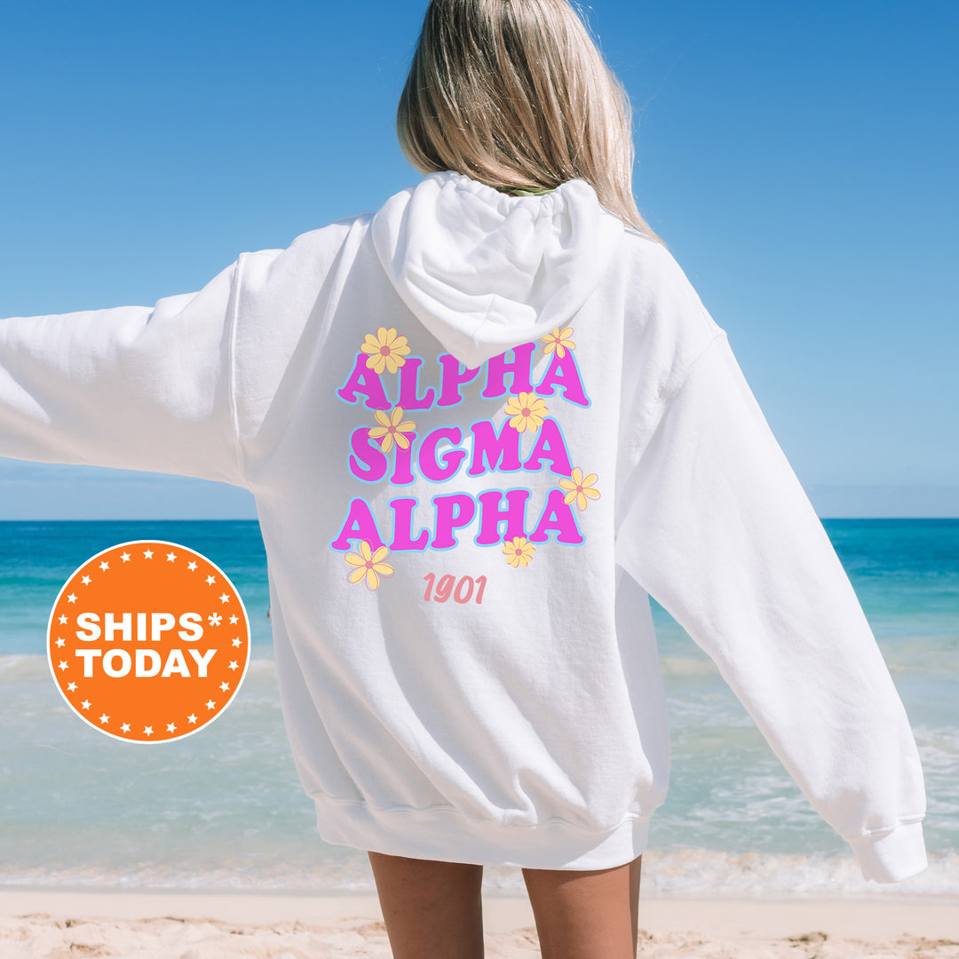 A woman wearing a white hoodie with the text "ALPHA SIGMA ALPHA" printed on it, standing on a beach with the ocean in the background.