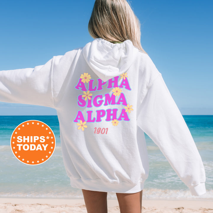 A woman wearing a white hoodie with the text "ALPHA SIGMA ALPHA" printed on it, standing on a beach with the ocean in the background.