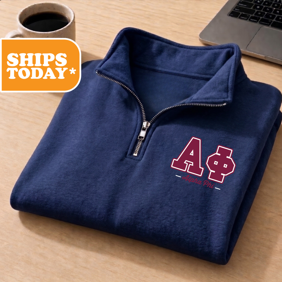 A navy blue zip-up jacket with the letters "AΠΟΣ" printed on it, placed on a wooden surface next to a laptop.
