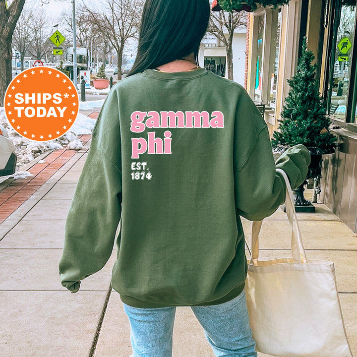 A person wearing a green sweatshirt with the text "gamma phi" printed on it, walking on a sidewalk.