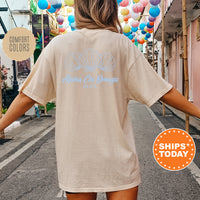 A person wearing a cream-colored t-shirt with a graphic design of seashells and the text 