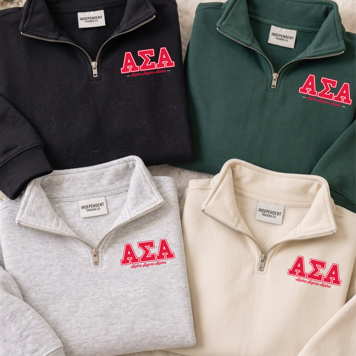 a collection of four zip-up sweatshirts, each with the Greek letters 'ΑΕΛΑ' printed on them. The sweatshirts are arranged in a row, with the first one being black, the second one being gray, the third one being green, and the fourth one being beige. Each sweatshirt has a label on the front, indicating that they are part of a collection or merchandise.