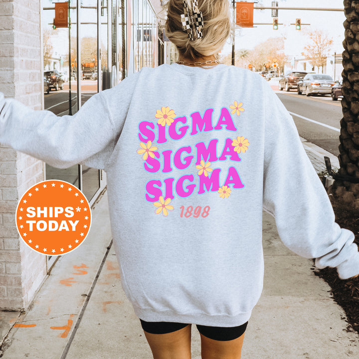 A person wearing a gray sweatshirt with the text "SIGMA SIGMA SIGMA" printed on it, standing on a sidewalk.