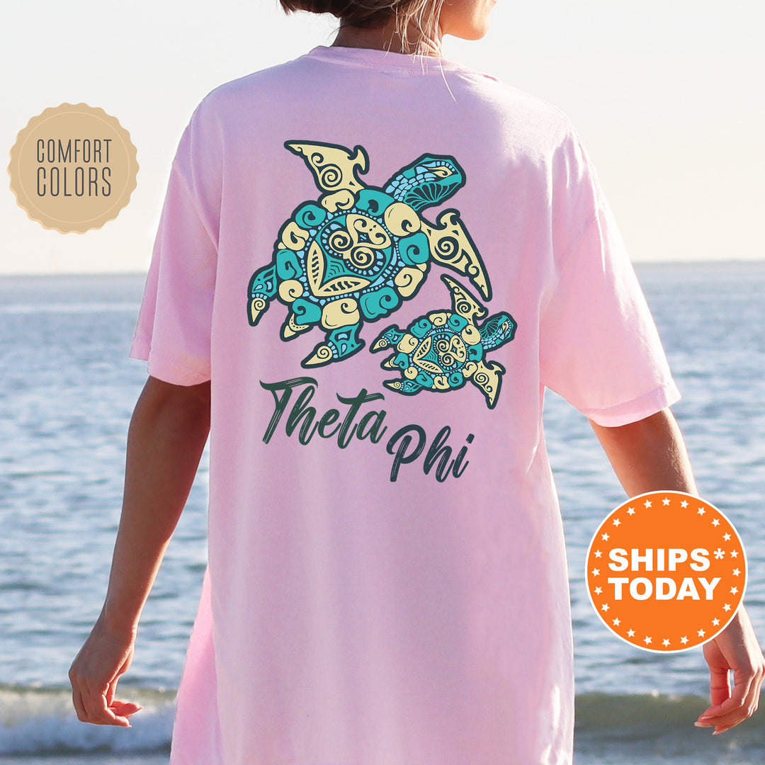 A person wearing a pink t-shirt with a design of two stylized turtles, one larger and one smaller, against a beach background.