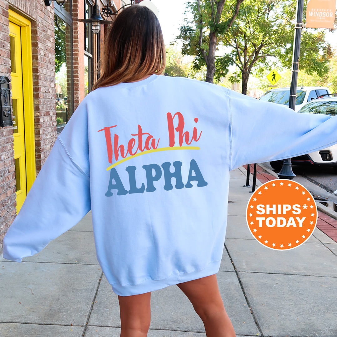 A woman wearing a light blue sweatshirt with the text "Theta Phi Alpha" printed on it, standing on a sidewalk.