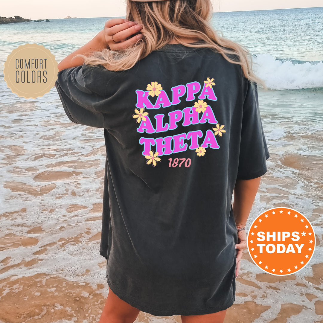A woman wearing a black t-shirt with the text "KAPPALETA THETA" printed on it, standing on a beach with waves in the background.