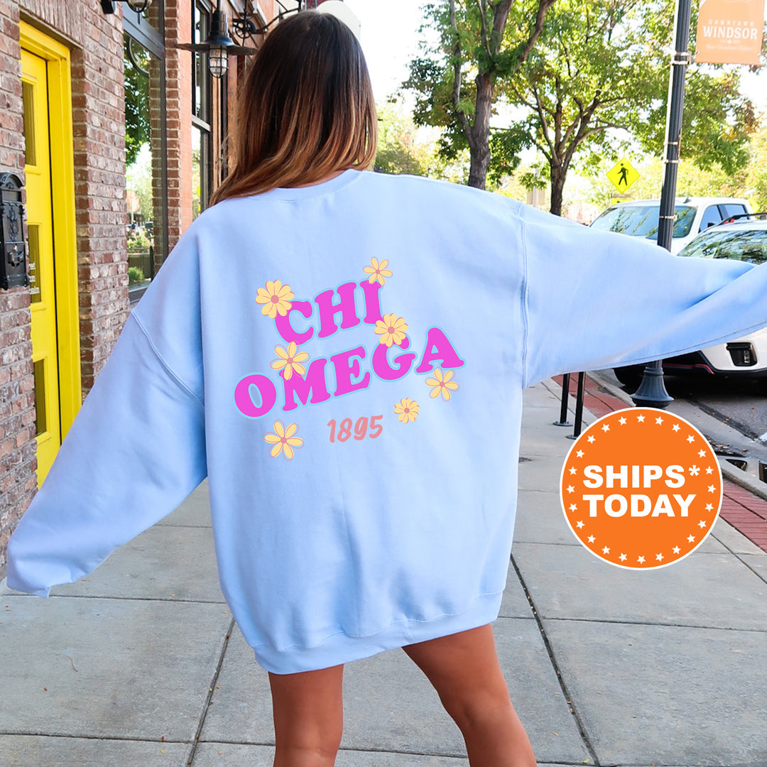 A woman wearing a light blue sweatshirt with the text "CHI OMEGA 1895" printed on it, standing on a sidewalk.