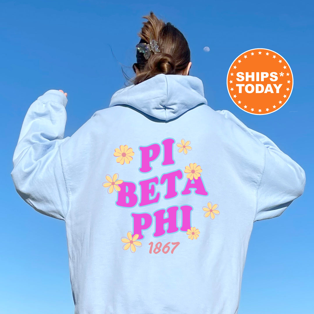A person wearing a light blue hoodie with the text "PI BETA PHI 1867" printed on it, standing against a clear blue sky.