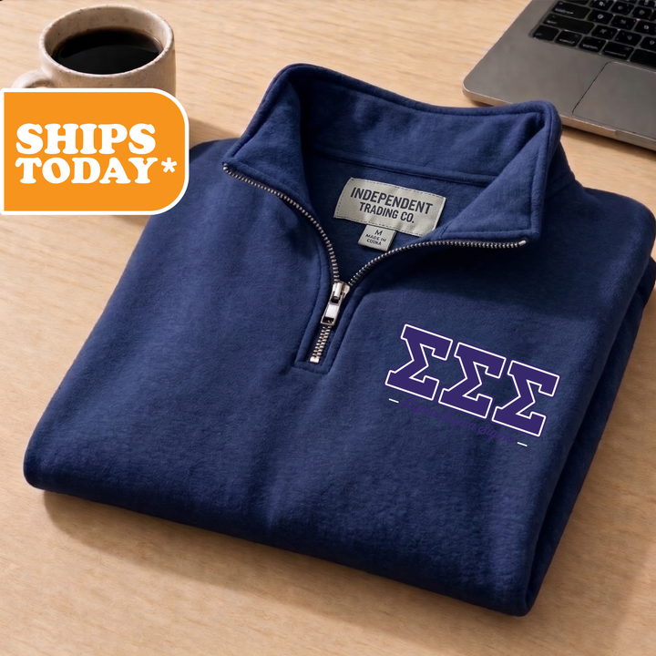 A navy blue zip-up jacket with a logo on the left chest, placed on a wooden surface next to a laptop and a coffee cup.