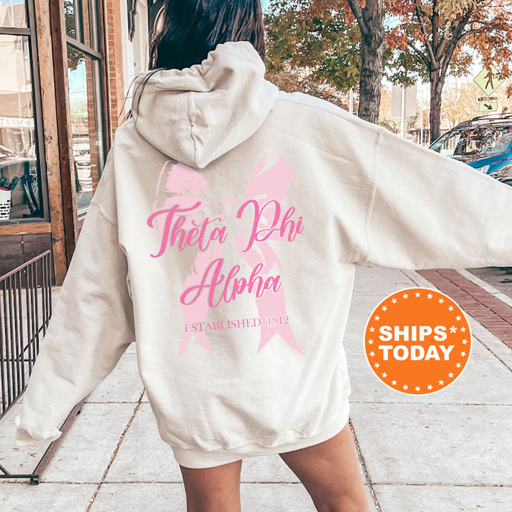 a woman walking down a sidewalk with a pink ribbon on her hoodie