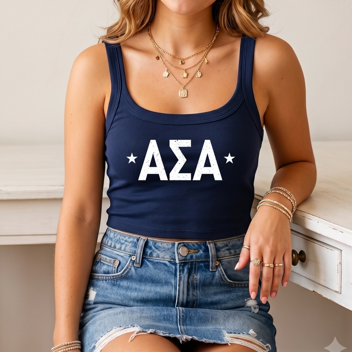 A woman wearing a navy blue crop top with white text and a denim skirt, sitting on a white surface.