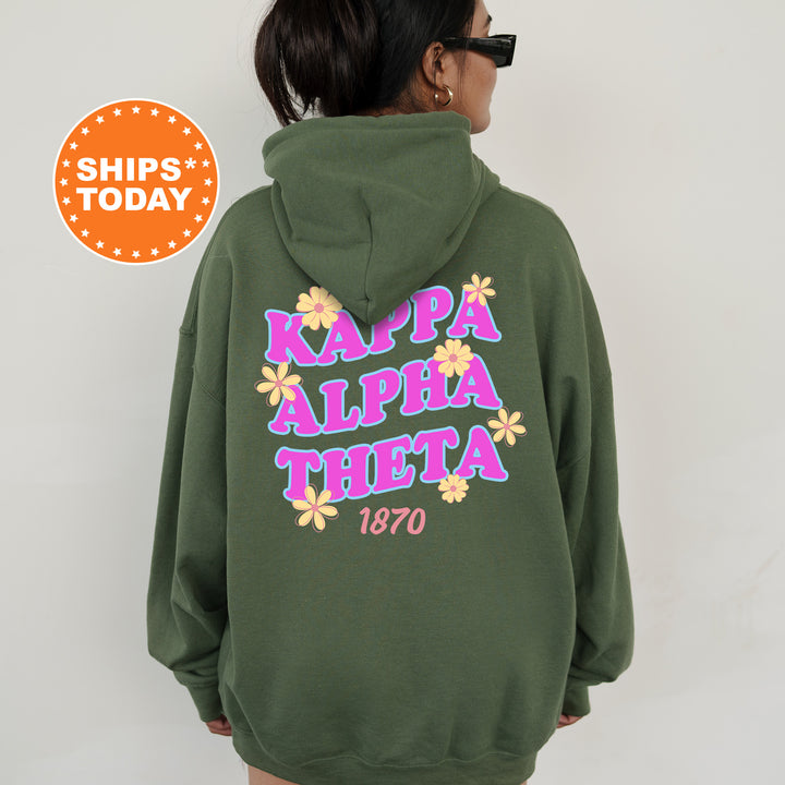A person wearing a green hoodie with the text "KAPPA ALPHA THEETA" printed on it, along with a floral design.