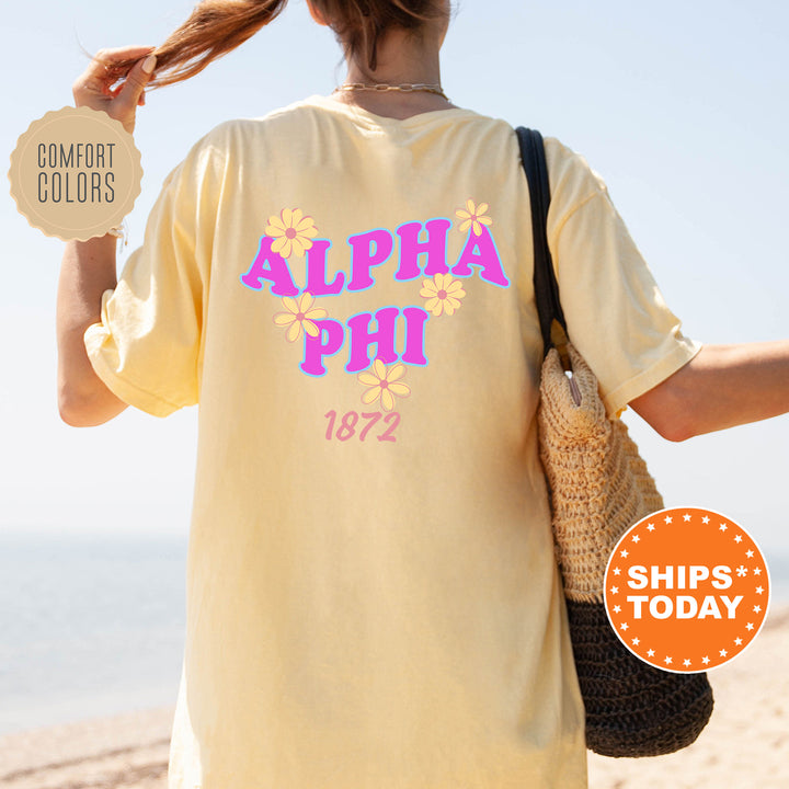 A person wearing a yellow t-shirt with the text "ALPA Phi 1872" printed on it, standing on a beach with a handbag.