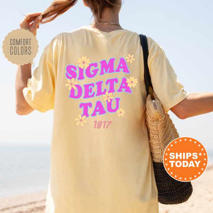 A woman wearing a yellow t-shirt with the text "SIGMA DELTA TAU" printed on it, standing on a beach.