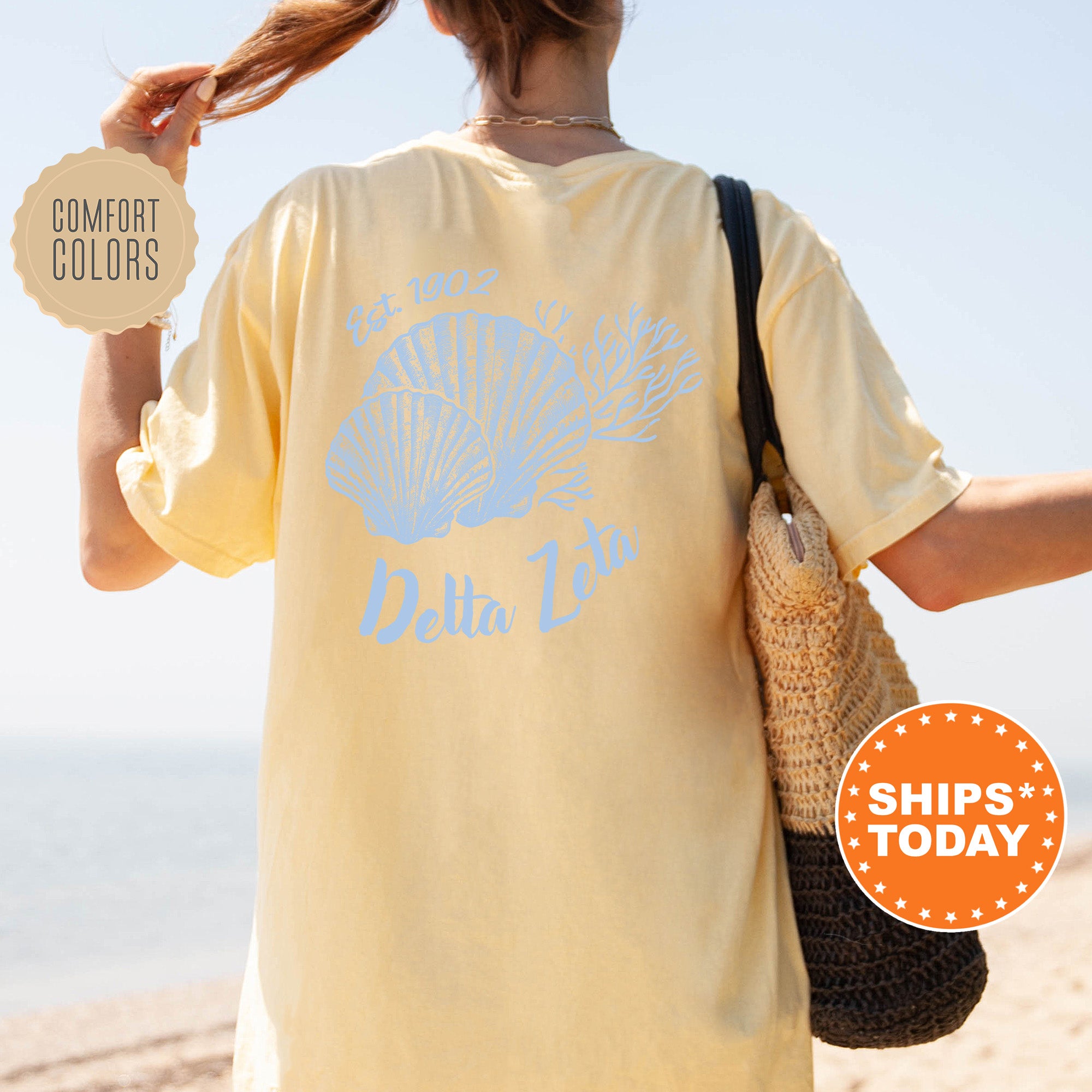 A person wearing a yellow t-shirt with a blue design and text, standing on a beach with a handbag and a sign advertising 
