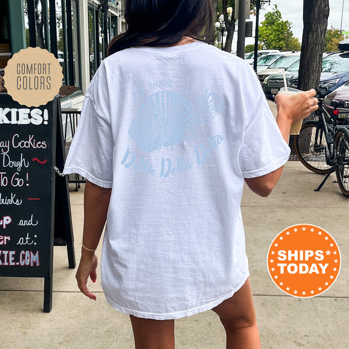 A person wearing a white t-shirt with a graphic design is walking on a sidewalk, with a chalkboard sign and bicycles visible in the background.