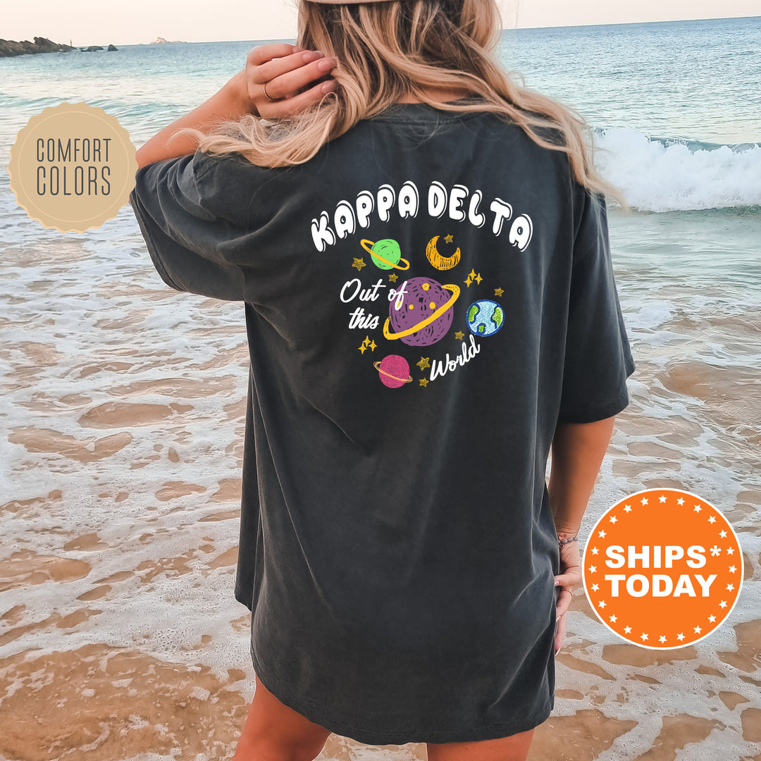 A woman wearing a black t-shirt with a colorful graphic design on the back, standing on a beach with the ocean in the background.