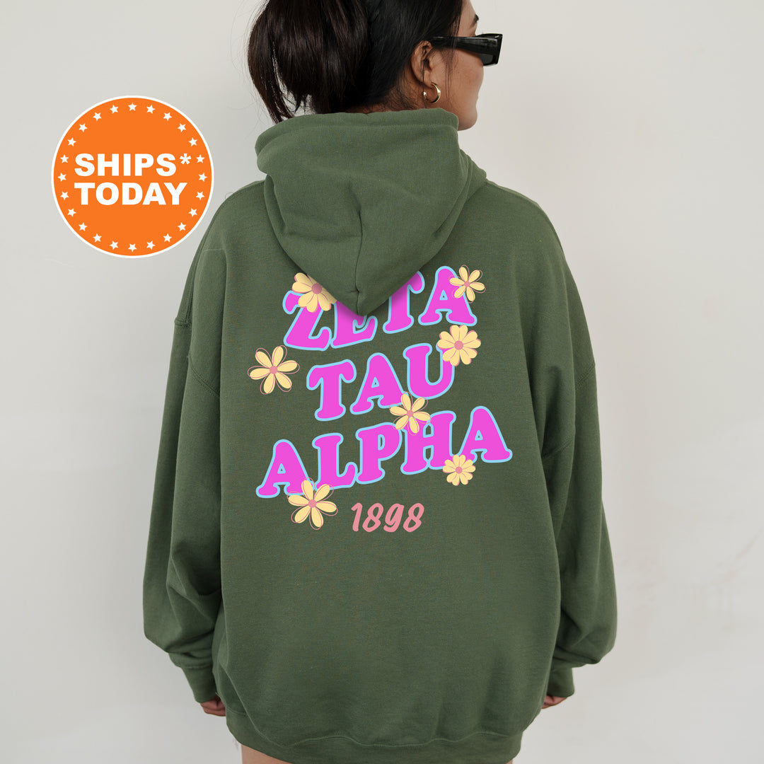 A person wearing a green hoodie with the text "ZETA TAU ALPHA" printed on it, along with a floral design.