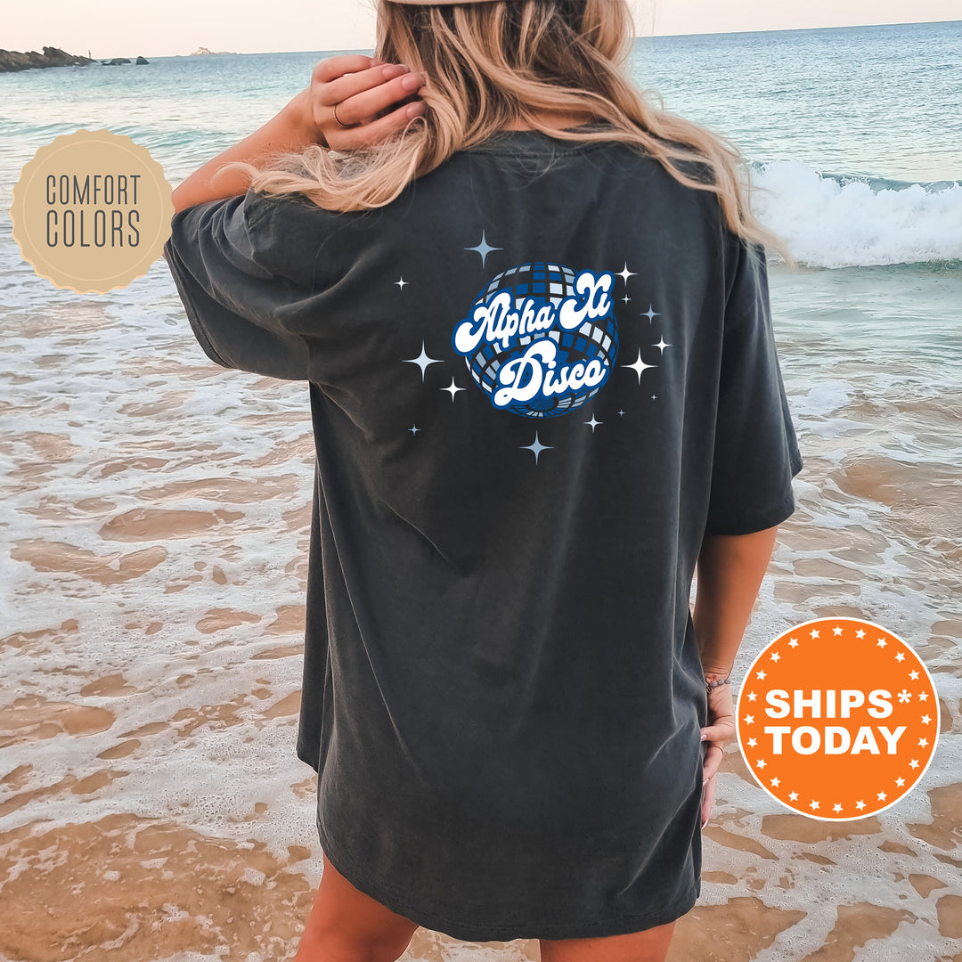 A woman wearing a black t-shirt with a graphic design on the back is standing on a beach, with the ocean and waves visible in the background.