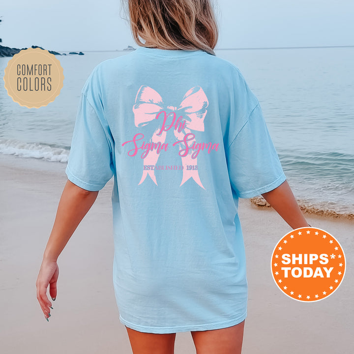 a woman walking on the beach wearing a blue shirt with a pink bow on it