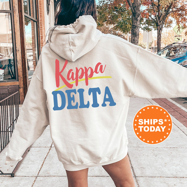A person wearing a white hoodie with the text " Kappa Delta" printed on it, standing on a sidewalk with a car and trees in the background.