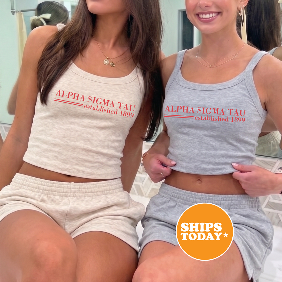 Two women wearing matching tank tops with the text "ALPA SIGMA TAU established 1899" are posing together.