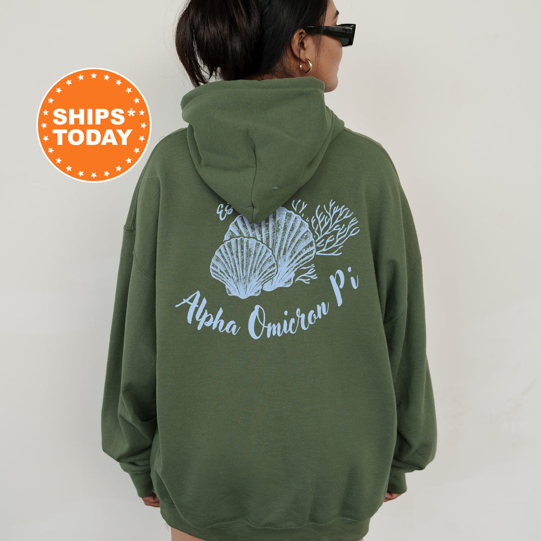 A person wearing a green hoodie with a graphic design of seashells and the text "Alpha Omega Pi" printed on it.