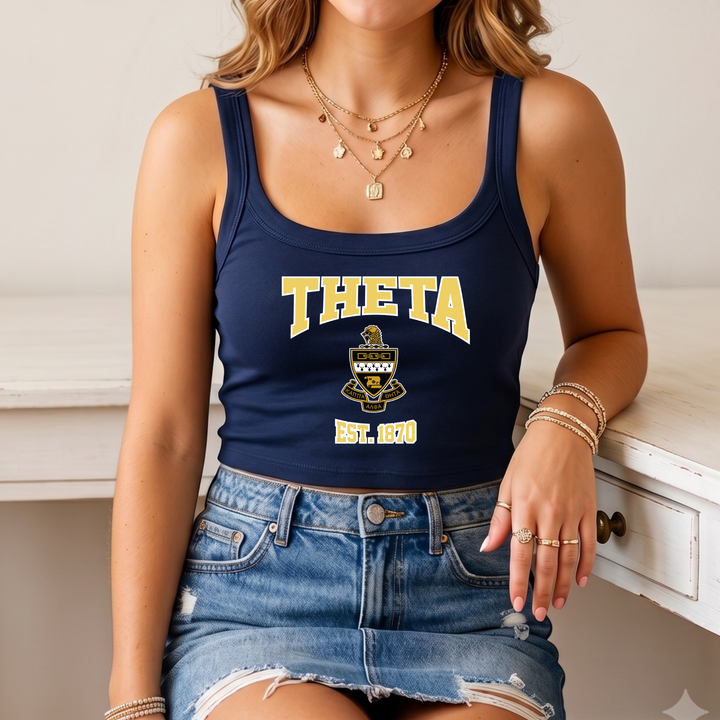A woman wearing a navy blue crop top with the text "THETA" and a graphic, paired with denim shorts and multiple rings on her fingers.