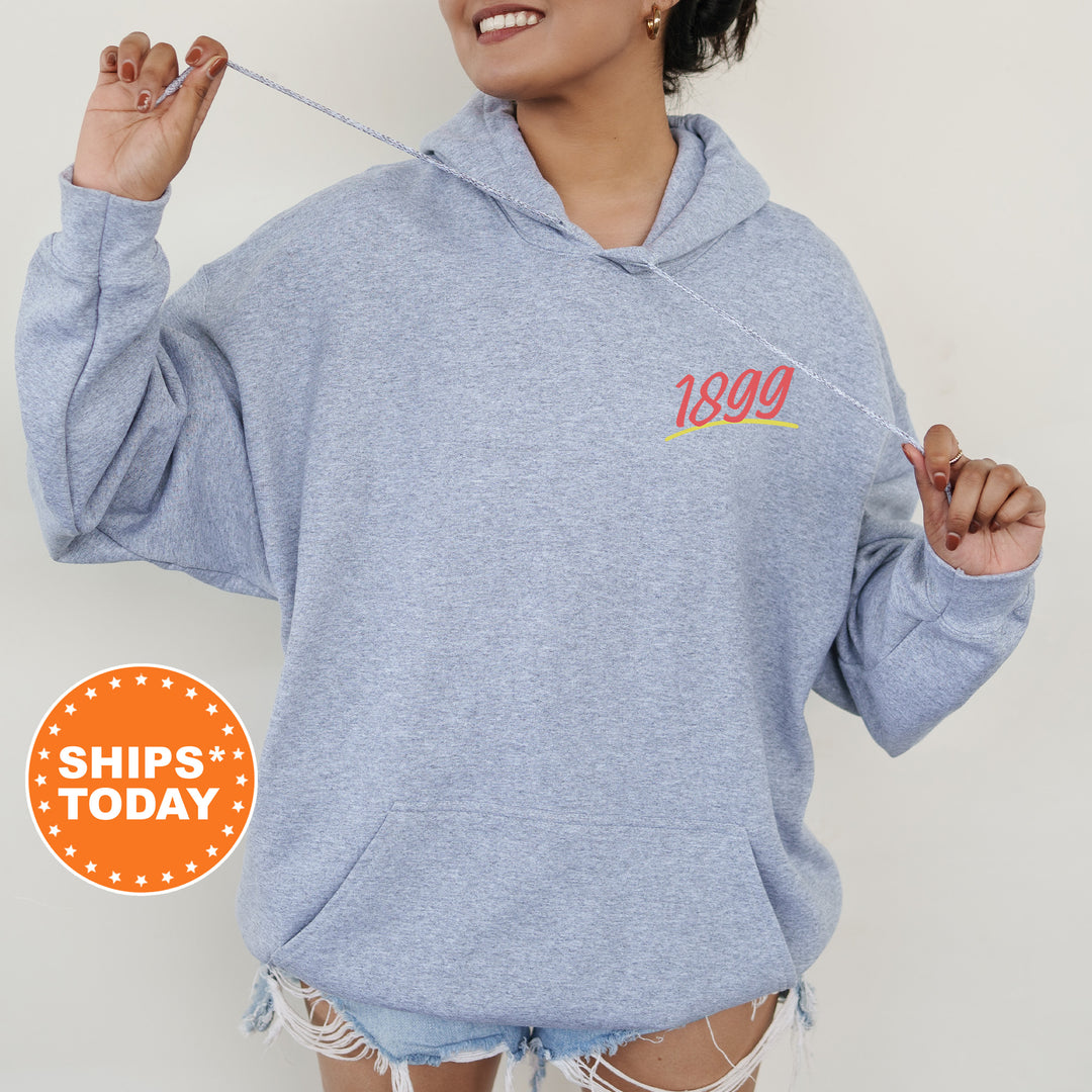 A woman wearing a gray hoodie with the number "1899" printed on it, smiling and holding a string.