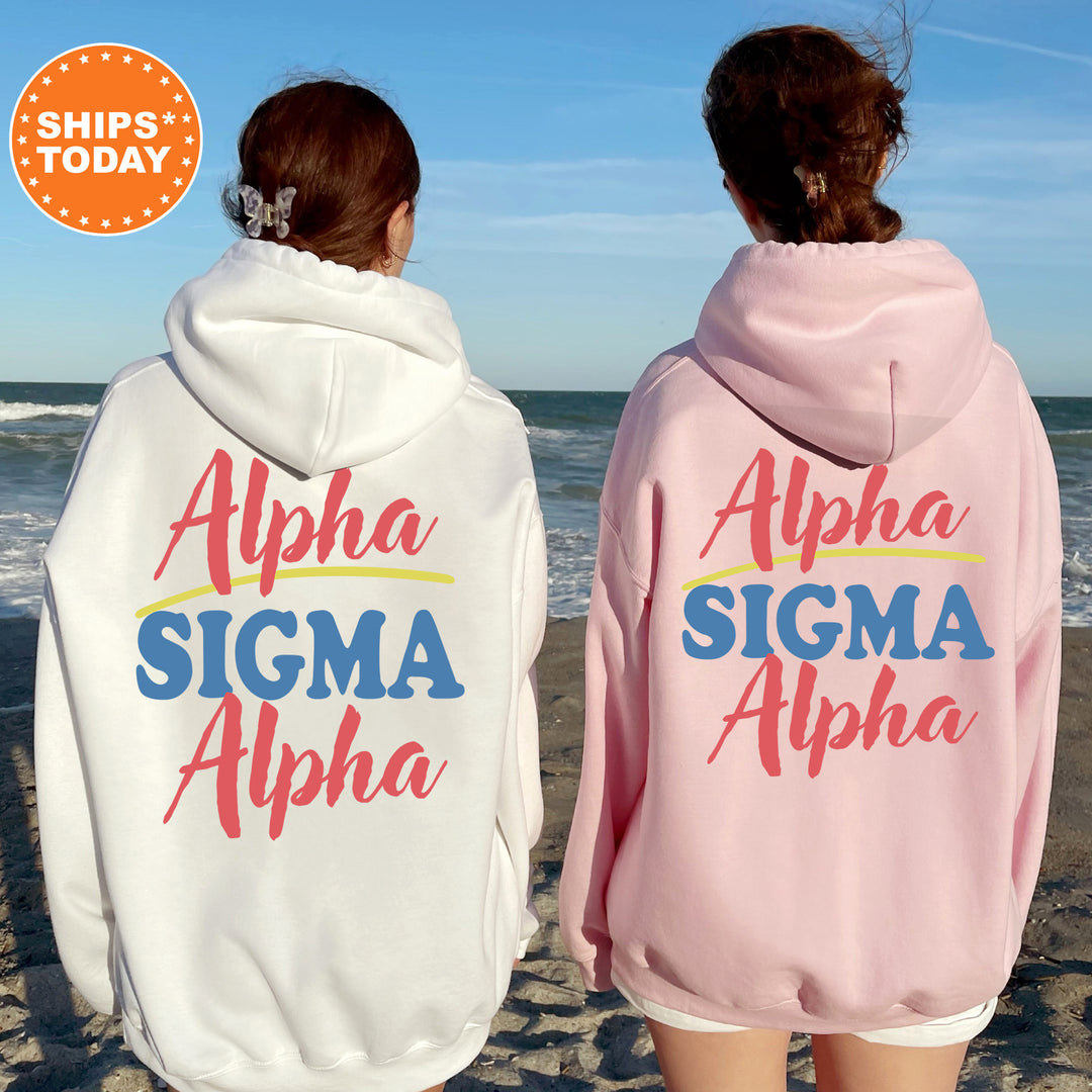Two women wearing matching "Alpha Sigma Alpha" hoodies stand on a beach, facing the ocean.