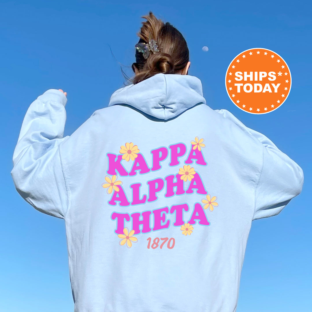 A person wearing a light blue hoodie with the text "KAPPAN ALPHA THEETA 1870" printed on it, standing against a clear blue sky.