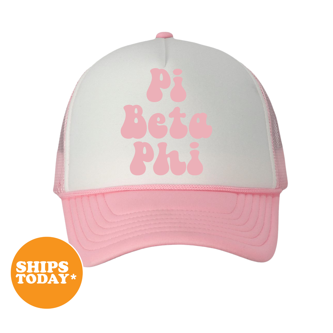 A pink and white baseball cap with the text "Pi Beta Phi" printed on it.